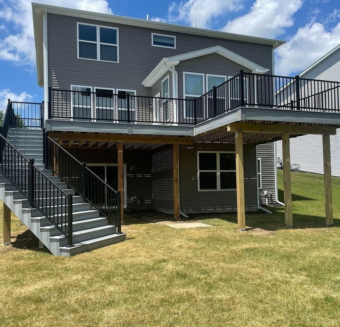 Two-story house with a gray exterior and a large deck with black railings and stairs.