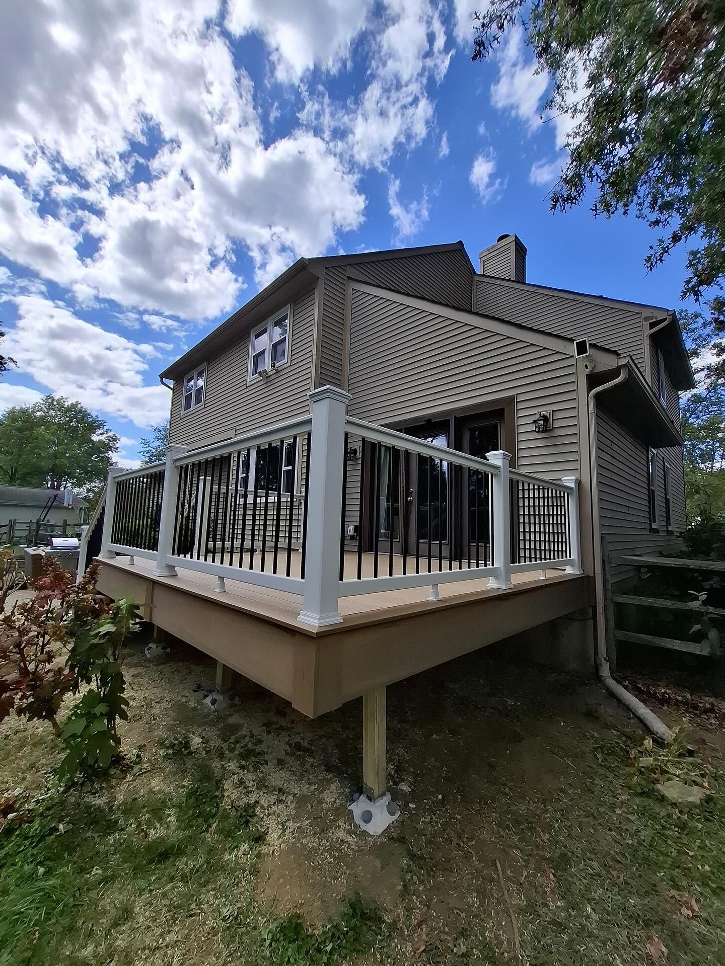 Wooden deck with black railings attached to a two-story house, set against a blue sky.