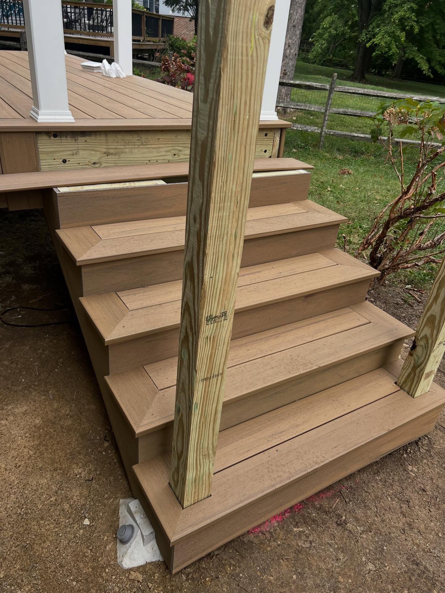 Brown composite deck stairs leading up to a deck with a wooden support post.