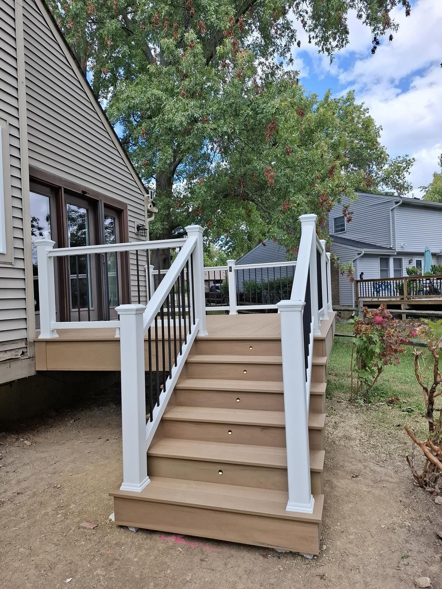 Wooden deck with white and black railings, stairs leading to a house. Outdoors, daytime.