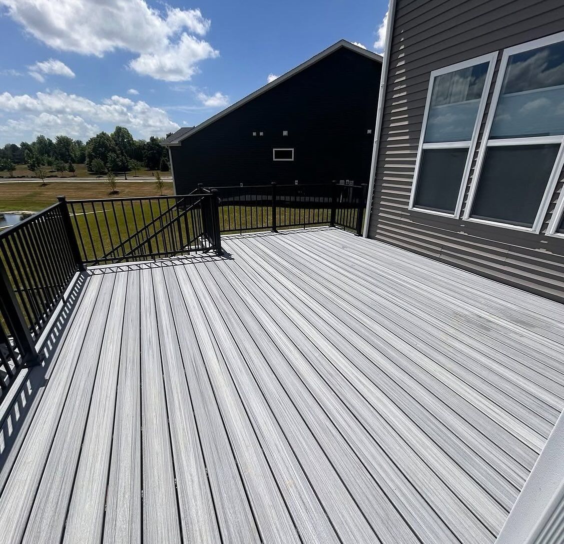 Gray composite deck with black railings, a dark house in the background, and a partly cloudy sky.
