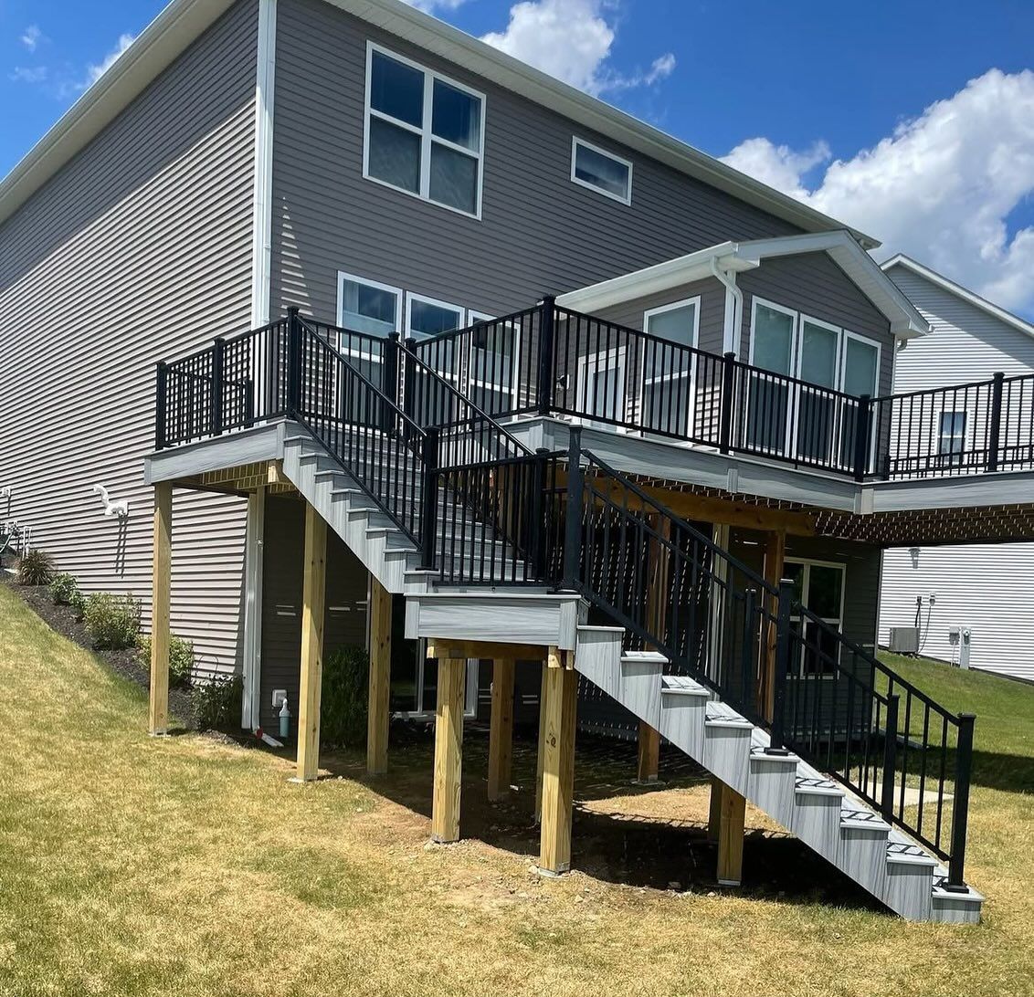 Two-story gray house with a deck and stairs, black railing, and grass in the yard.