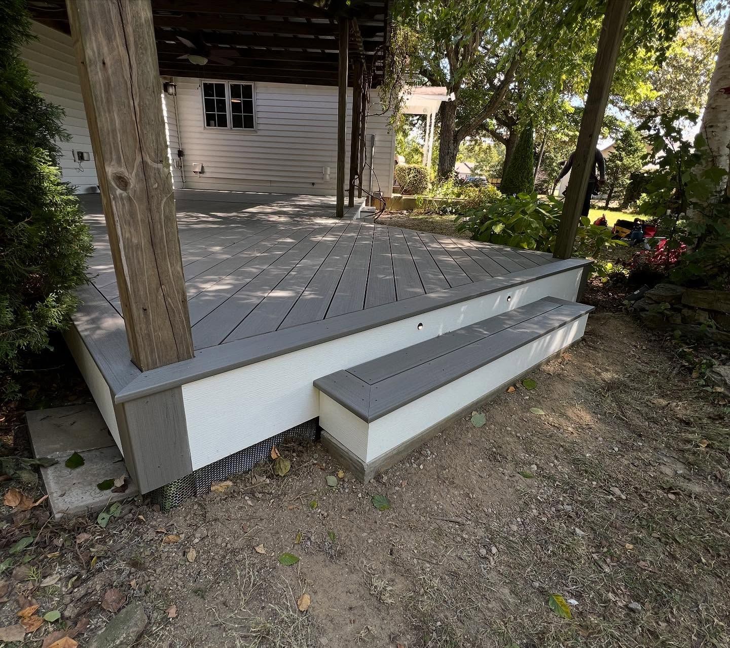 Grey composite deck with white trim and steps, surrounded by trees and dirt.