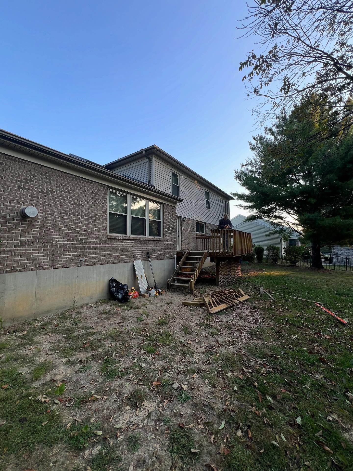 Backyard with a two-story house. Brick siding on left, deck and trees on right.