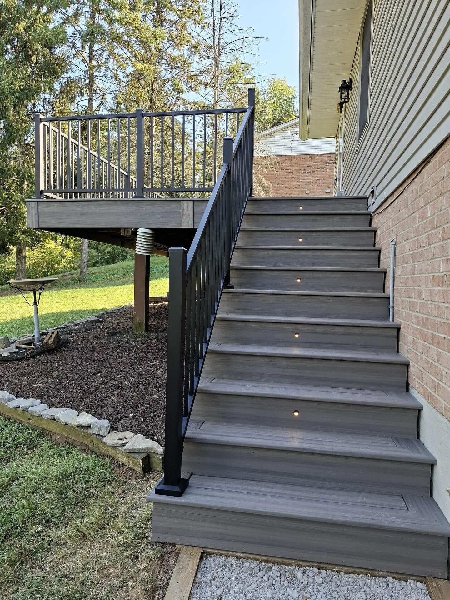 Grey composite deck stairs with black railing, leading up to a deck attached to a house.