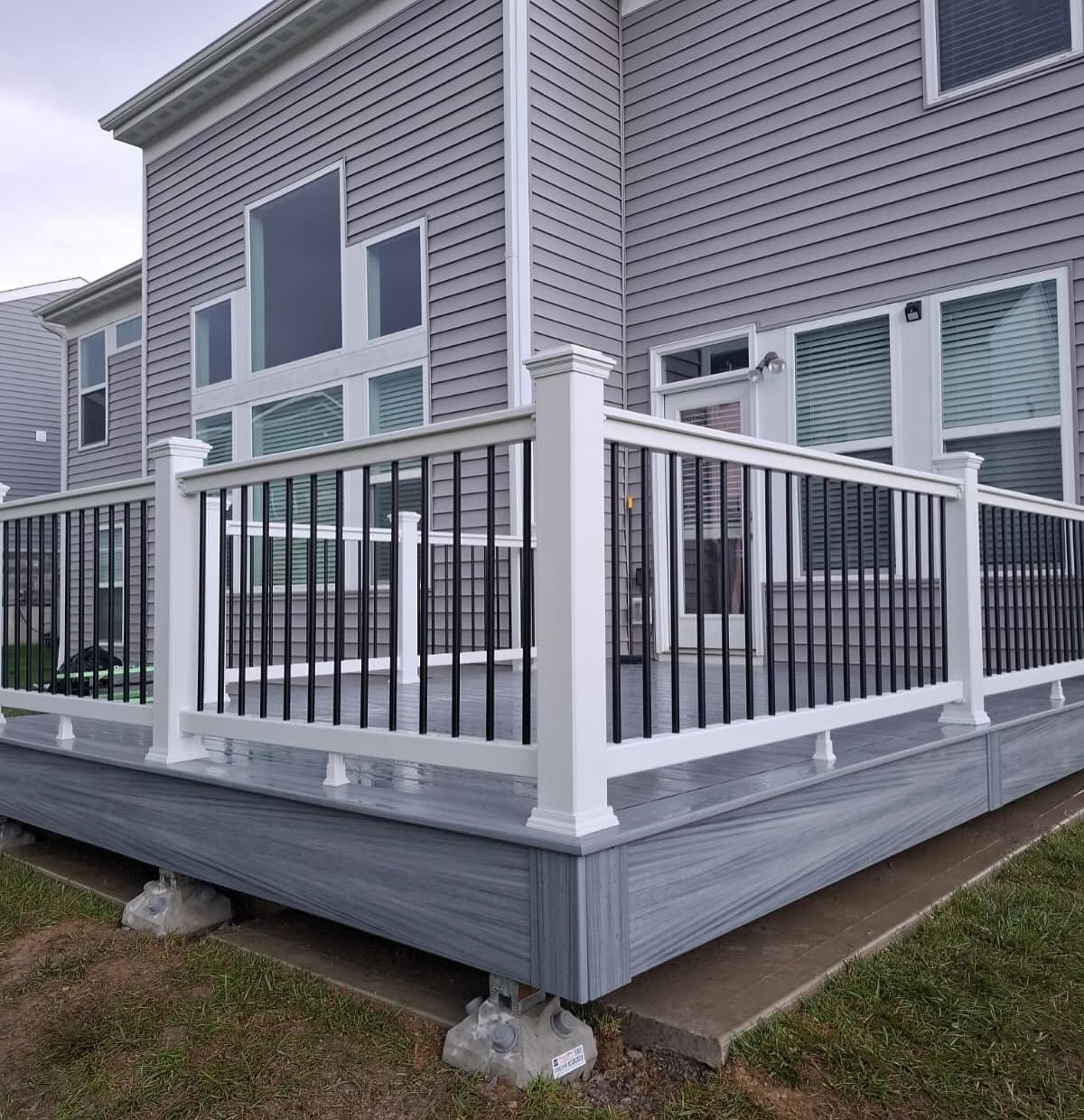 Grey composite deck with white railing, black balusters, and a house in the background.