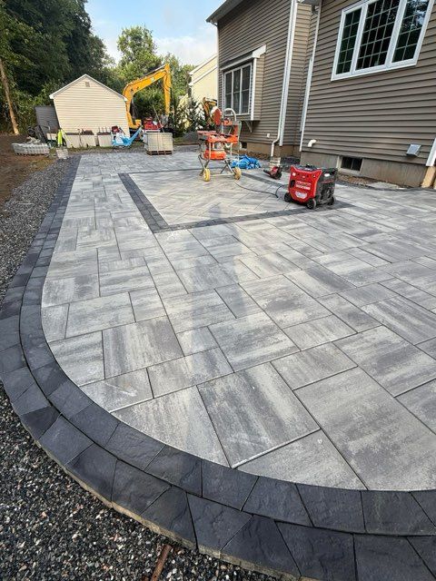 Gray composite deck with stairs, attached to a two-story house with brick and siding, sunny outdoors.