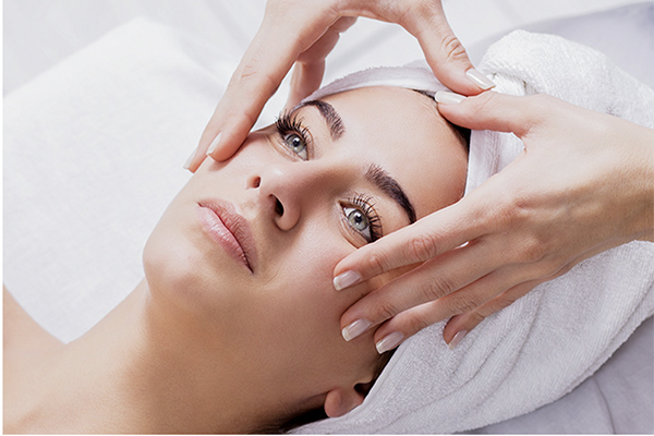 Femme recevant un soin du visage, les mains massant son visage, se relaxant avec une serviette sur la tête.