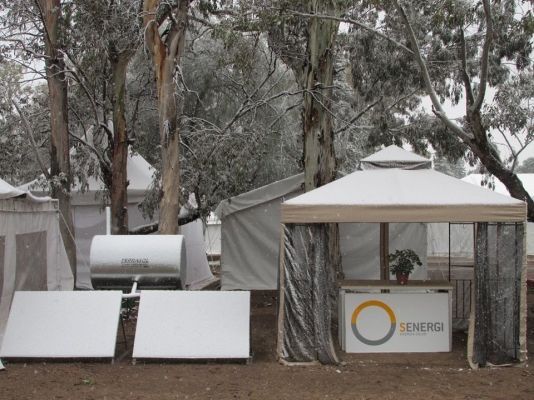 Paneles solares y cabina cubiertos de nieve, frente a los árboles.