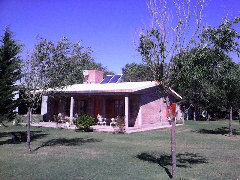 Casa de ladrillo con porche cubierto, paneles solares en el tejado y césped verde.
