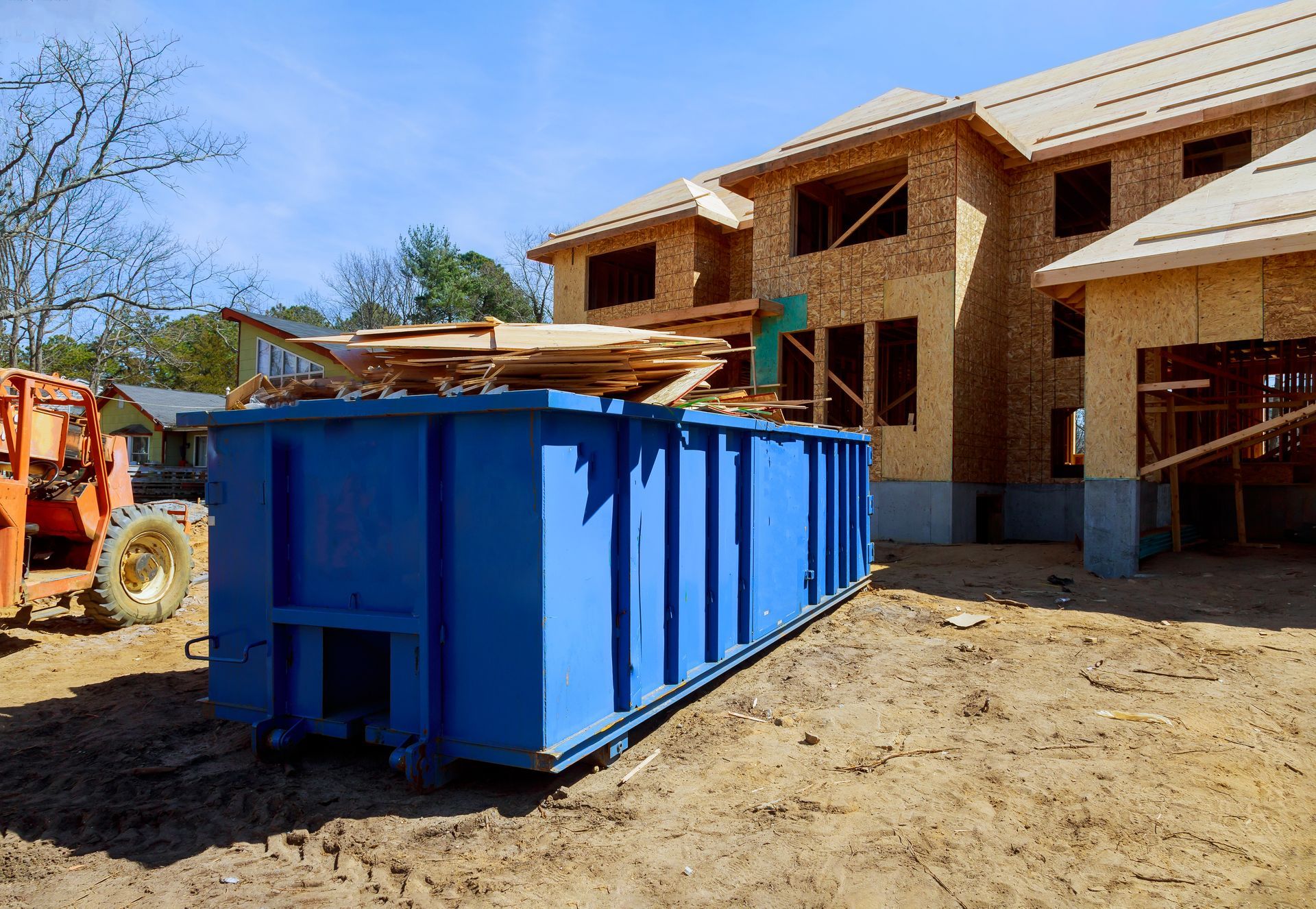 A blue dumpster is sitting in front of a house under construction.