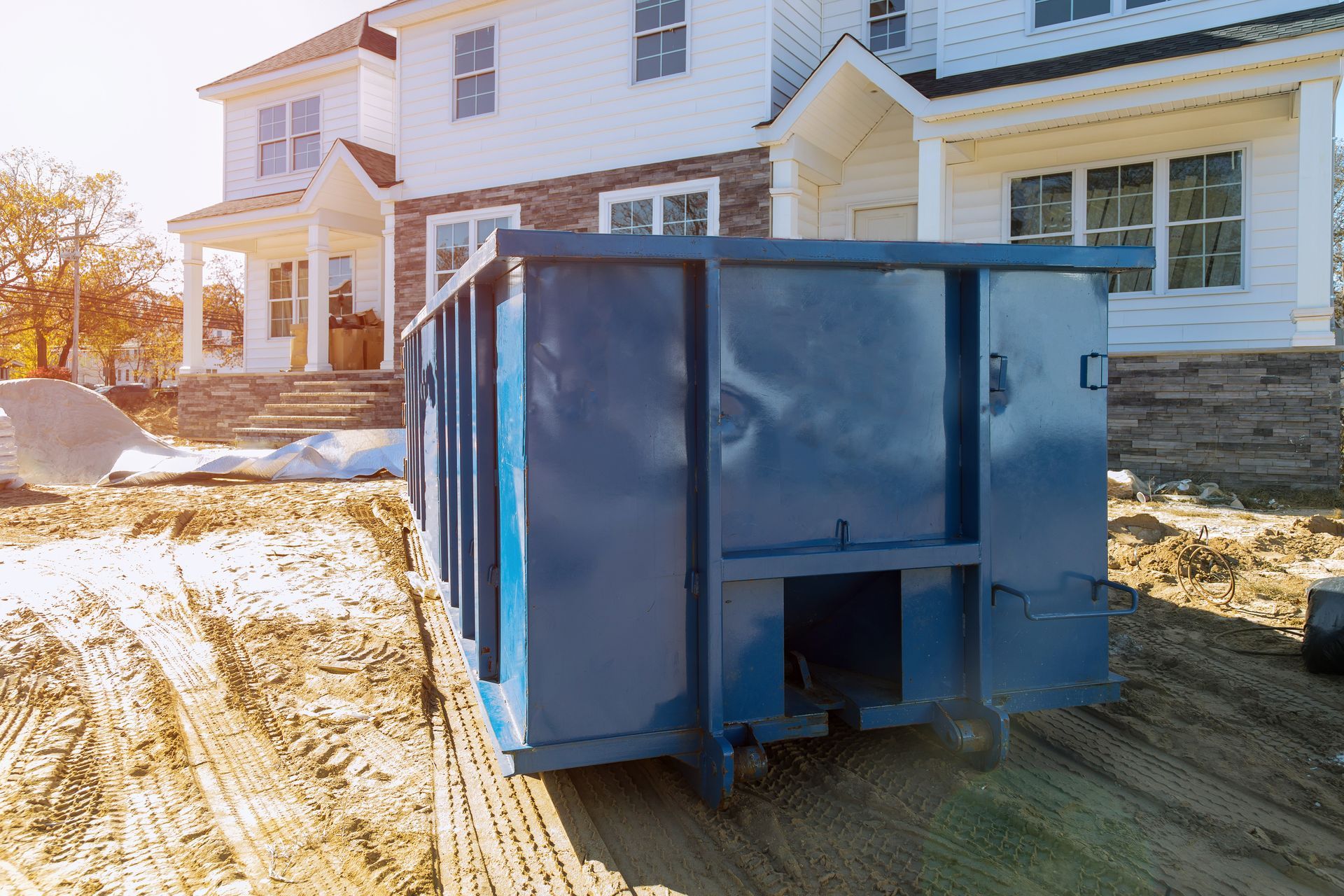 A blue dumpster is parked in front of a house under construction.