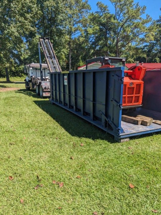 A dumpster is sitting in the grass next to a truck.