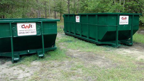 Two green dumpsters are parked next to each other in a grassy area.