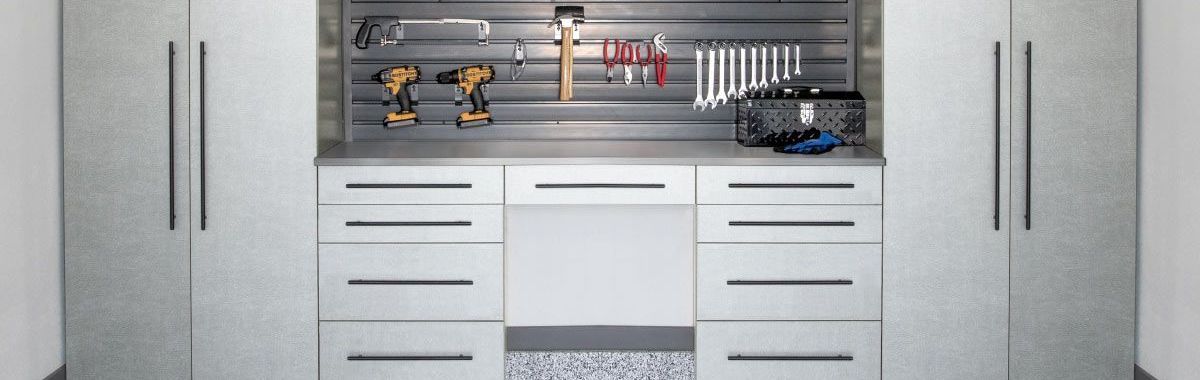 A garage with white cabinets and drawers and a workbench with tools on it.