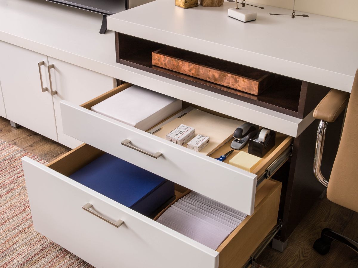 A desk with a drawer open filled with office supplies