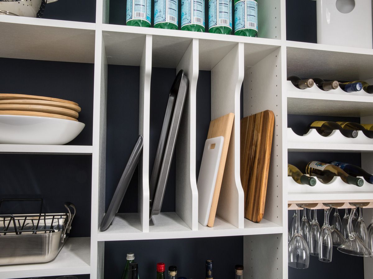 A pantry with bottles of water , cutting boards , tongs , and wine glasses.