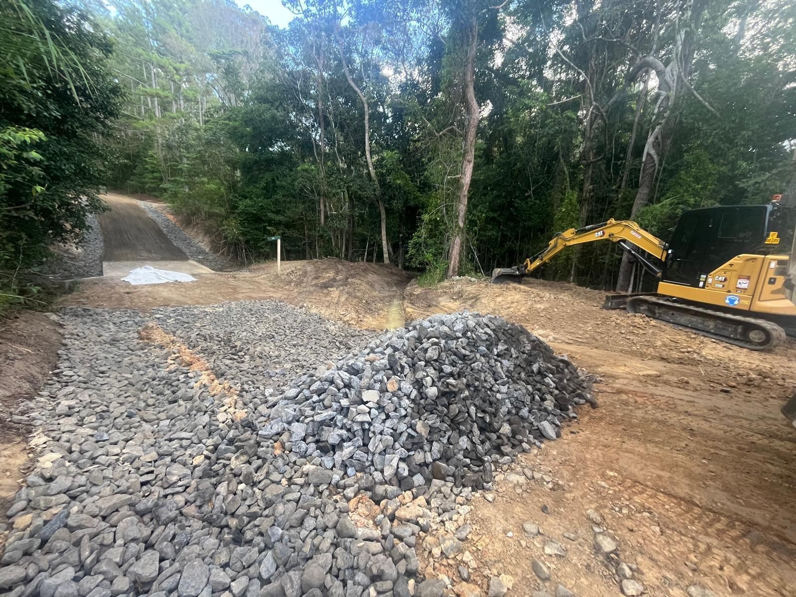 Gravel road under construction in a wooded area, with an excavator on the right and a small bridge in the distance — Kuranda Landscape Supplies in Kuranda, QLD
