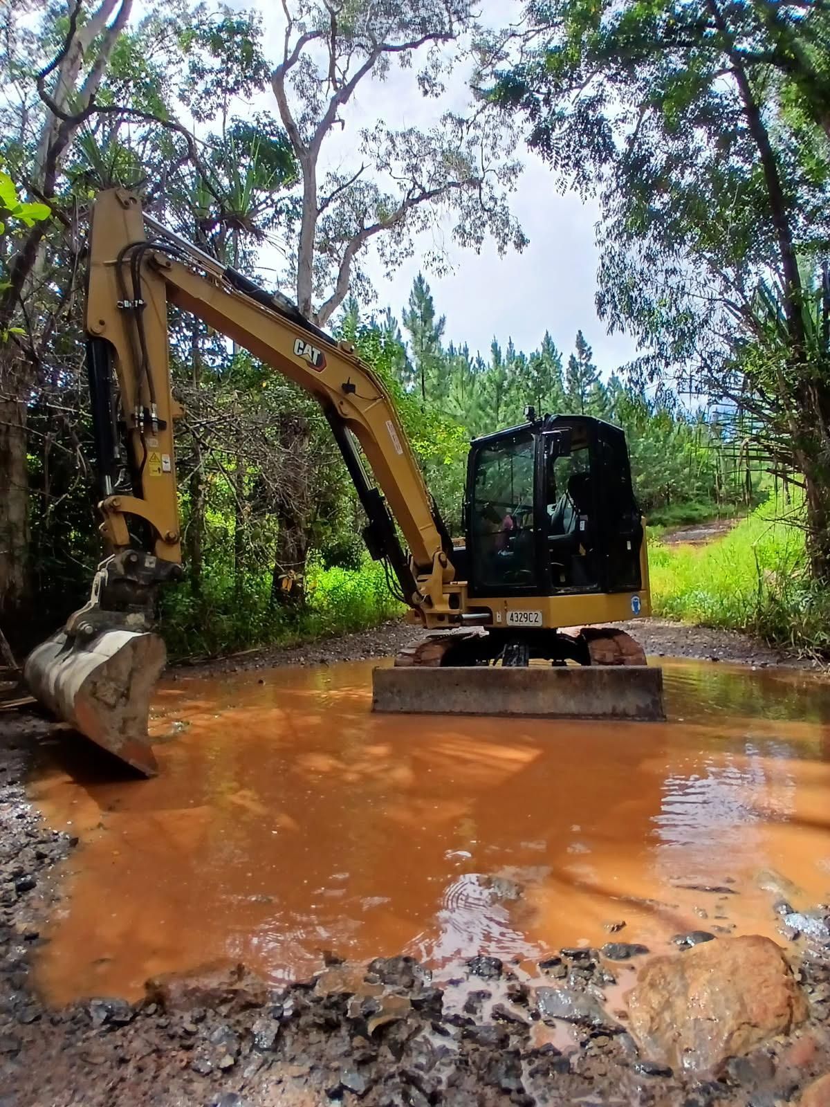 Yellow excavator in muddy water surrounded by trees — Kuranda Landscape Supplies in Kuranda, QLD