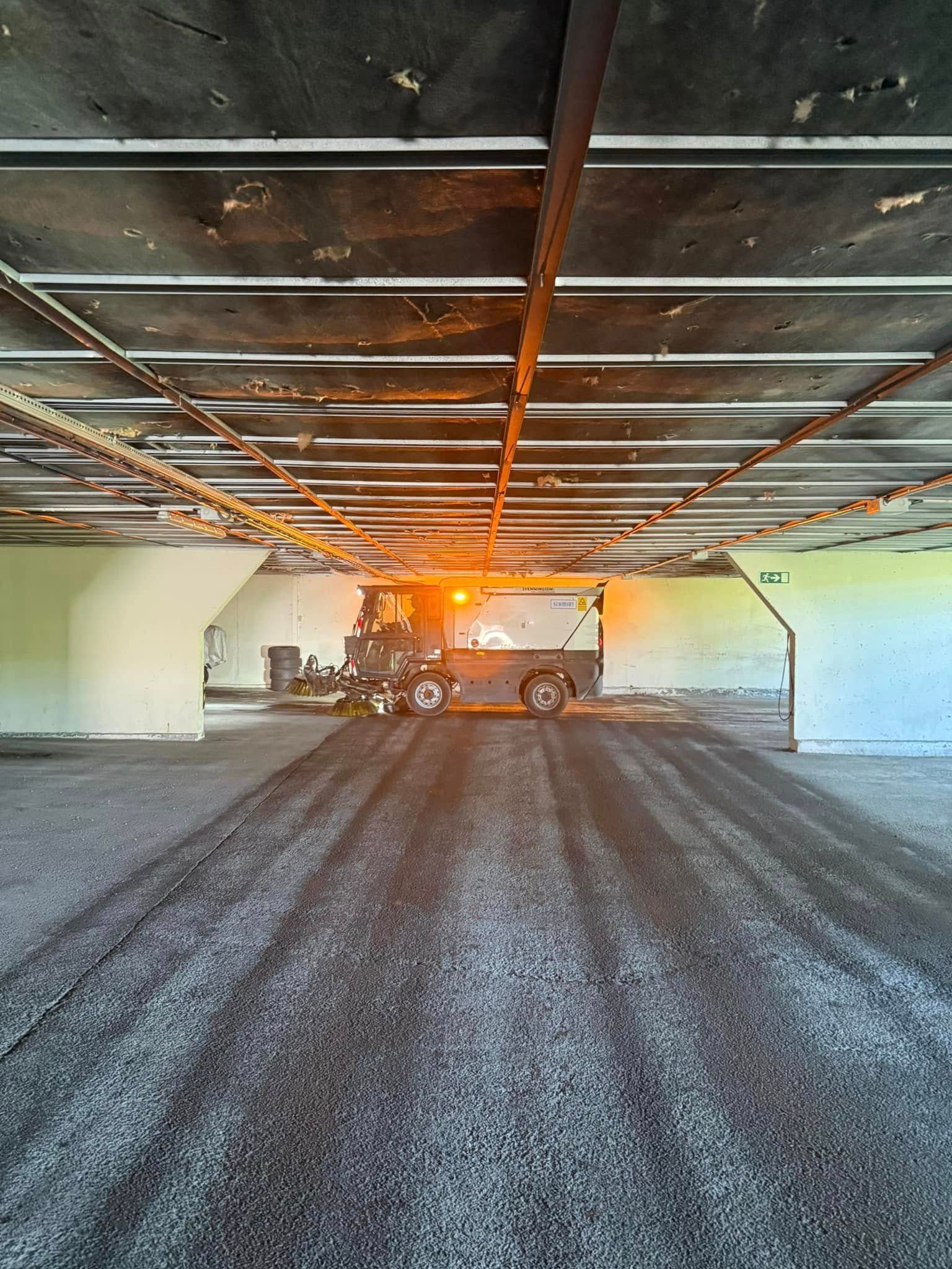 Tungt maskineri inne i en betongundergang, som glatter ut en mørk grusoverflate under sterke lys.