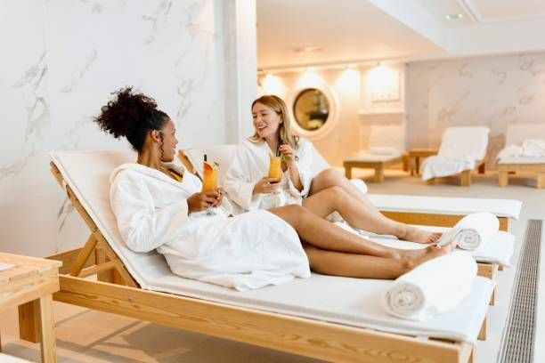Two people in white robes relaxing on lounge chairs, holding drinks, in a spa.