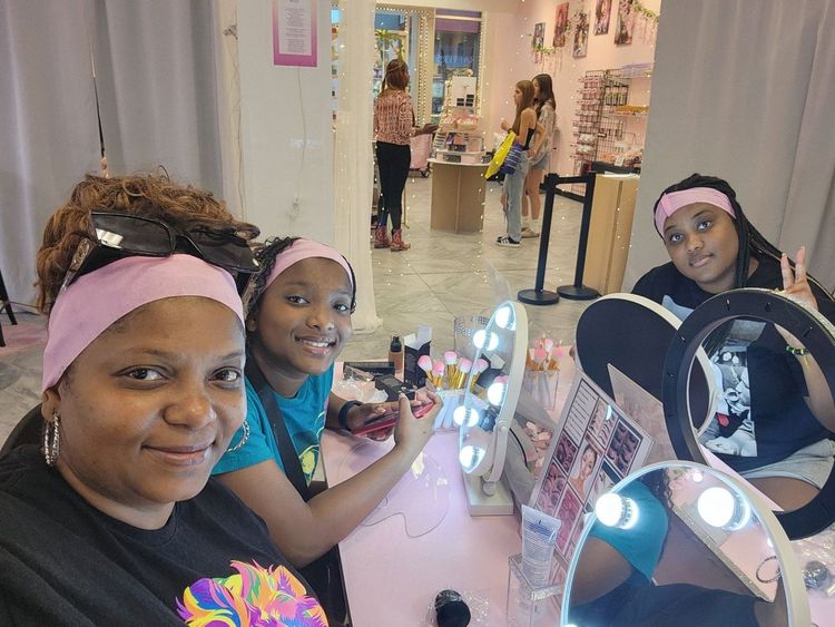 Five people lying on a bed with their legs raised. They wear white shirts, in a bright room with flowers.