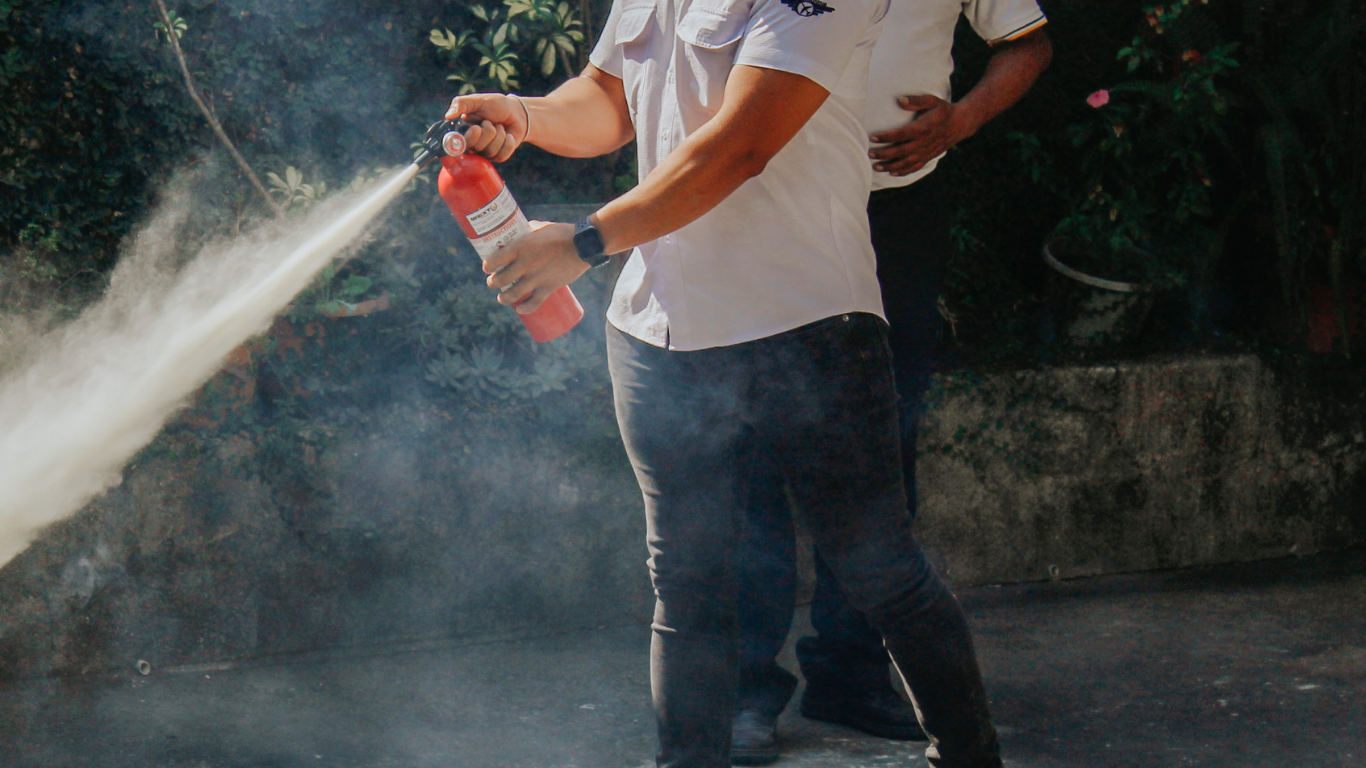 Person in white shirt and dark pants using a fire extinguisher, producing a cloud of white substance.