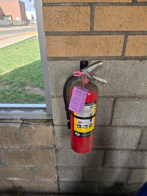 Three red fire extinguishers with a person in a blue uniform inspecting them with a clipboard.