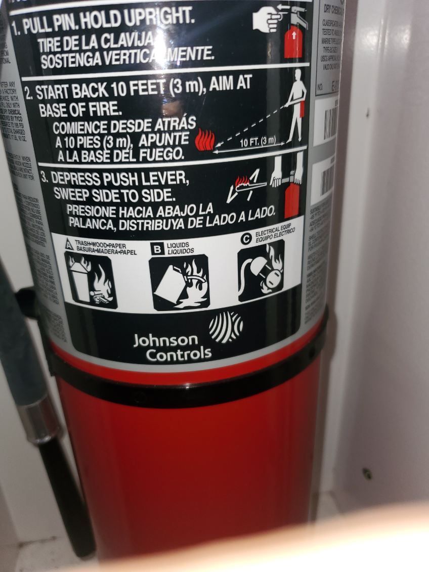 Red fire extinguisher in a brightly lit laboratory, set on a black countertop, near lab equipment.