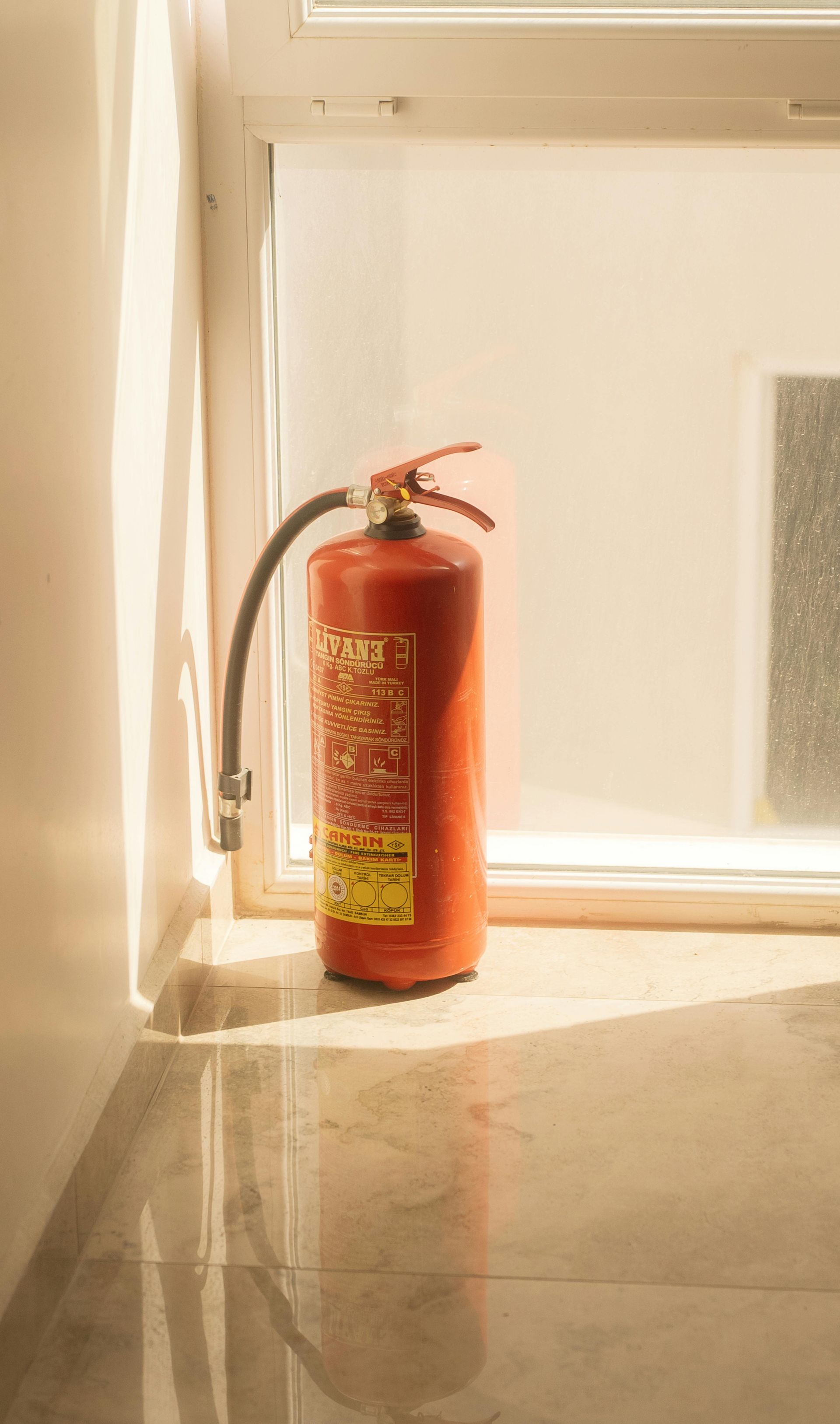 Red fire extinguisher by a window, indoors.