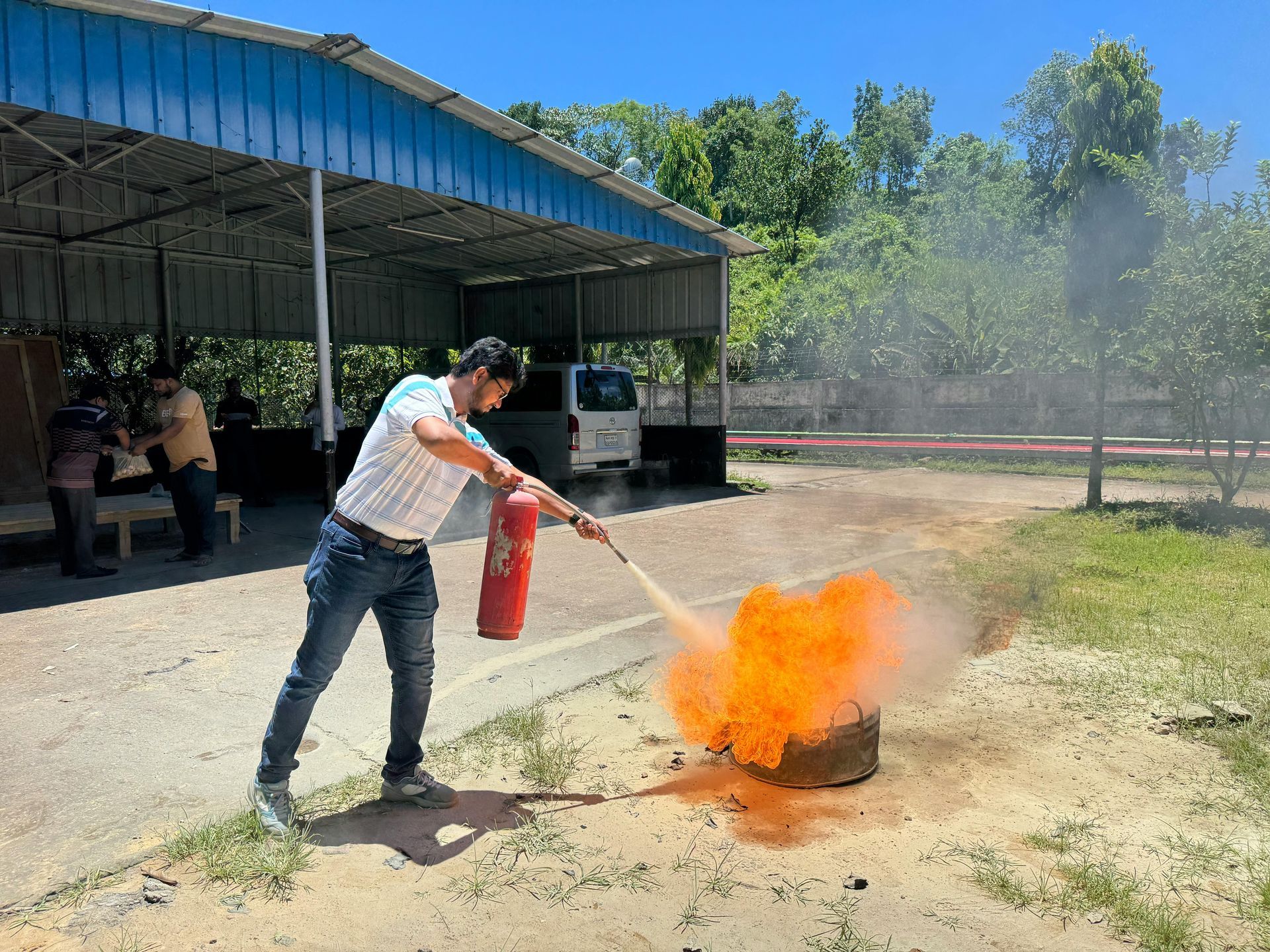 Person using a fire extinguisher on a burning barrel outdoors under a covered shed