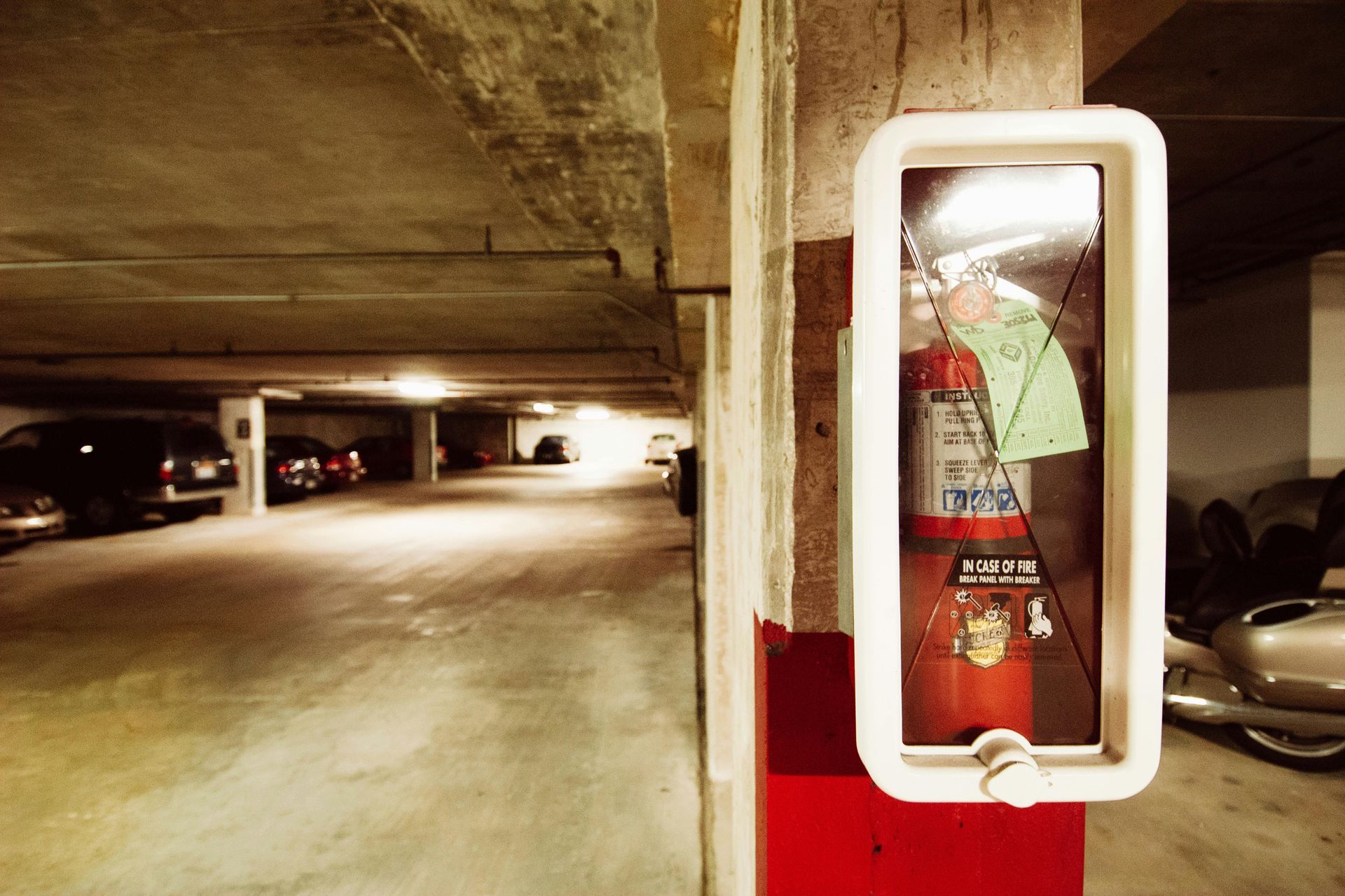 Parking garage with a red fire extinguisher cabinet on a concrete pillar and parked cars in the background