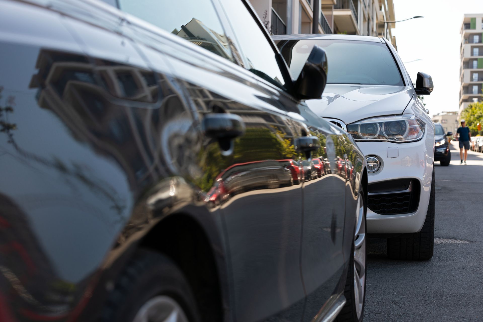 Black car parked next to white SUV on a city street. Buildings in background.