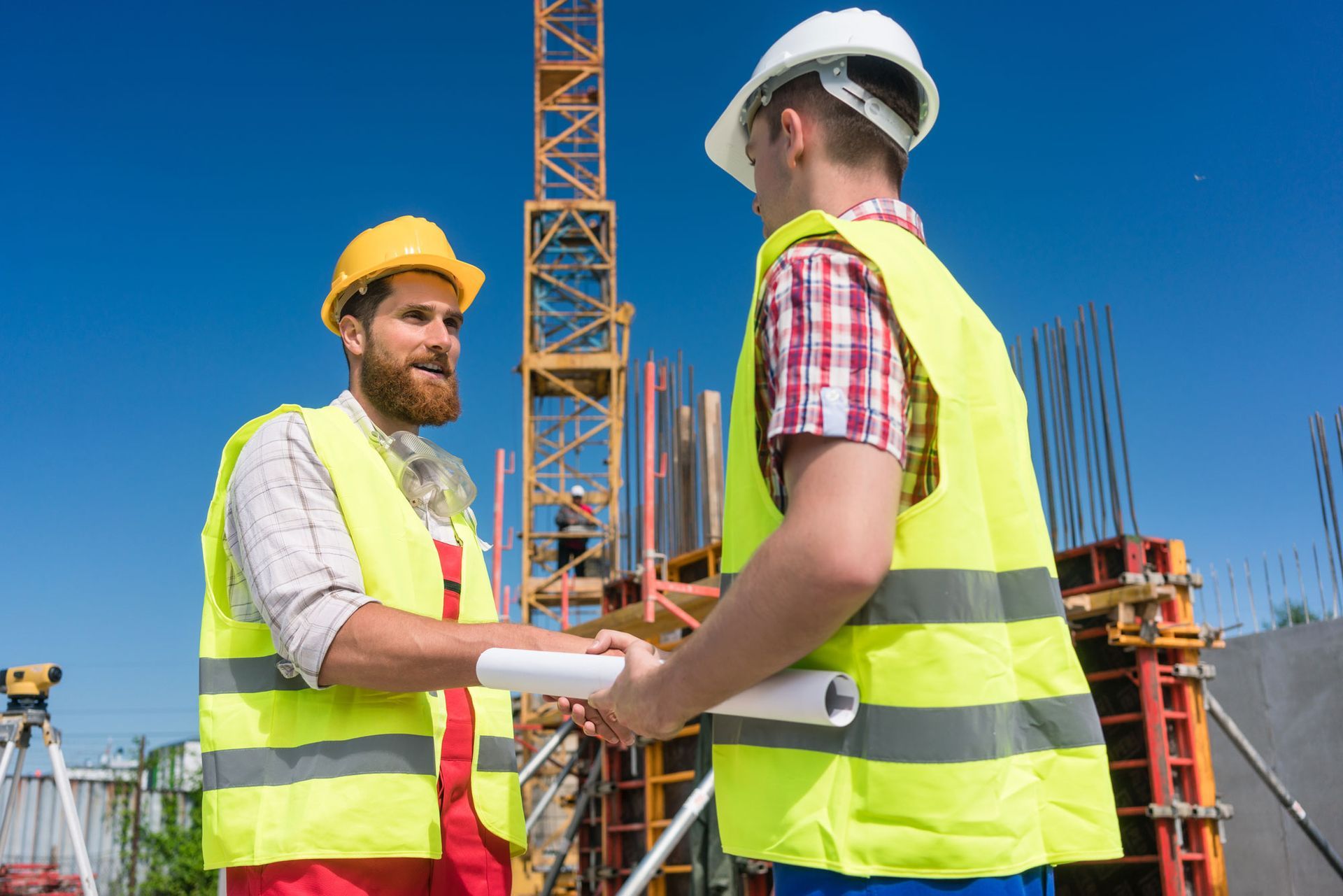 Two construction workers in safety vests shake hands on a construction site.