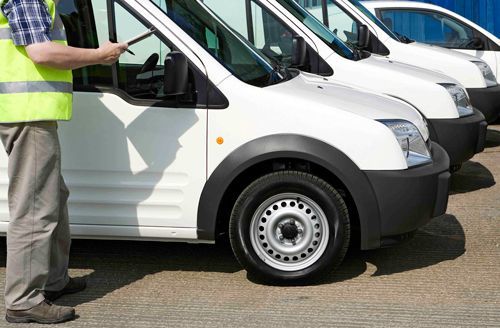 Man in safety vest checks white vans parked in a row.