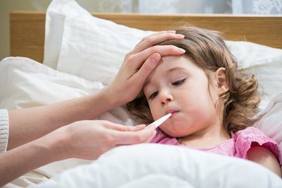 Adult checking a sick child’s temperature with a thermometer in bed
