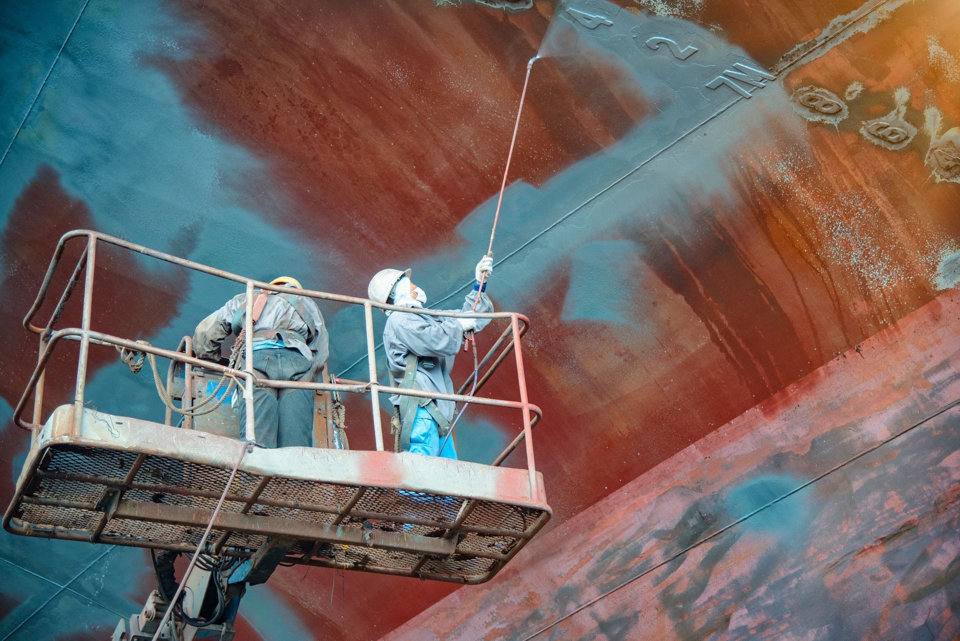 Two men are painting the side of a large ship.