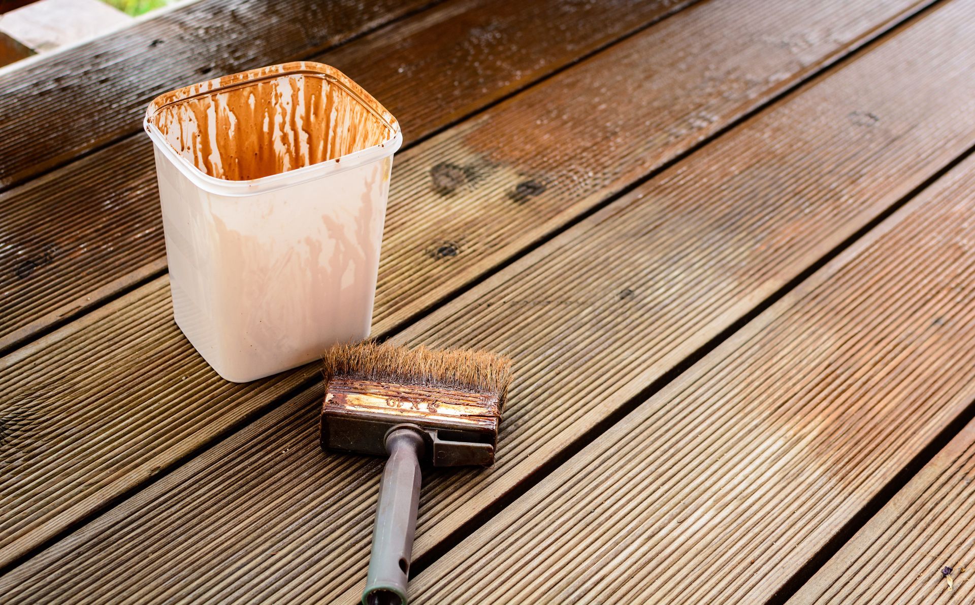A bucket of paint and a brush are sitting on a wooden deck.