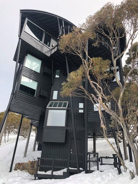 A black house is sitting on top of a snow covered hill.