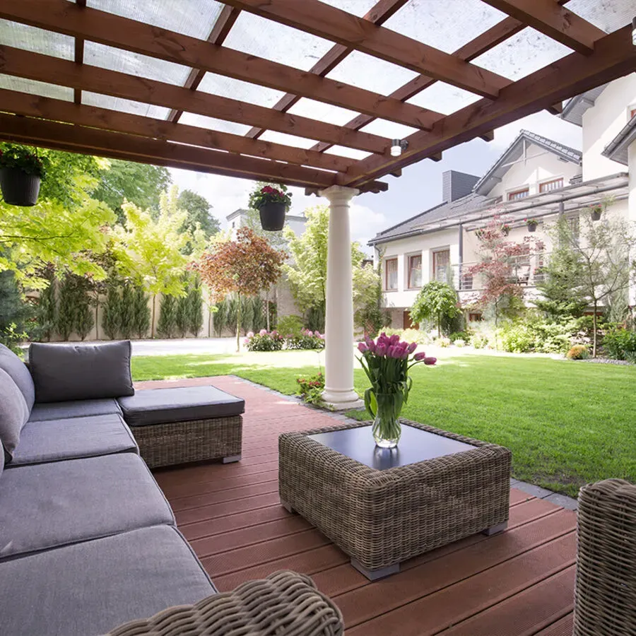 A patio with a couch , table and vase of flowers under a pergola.