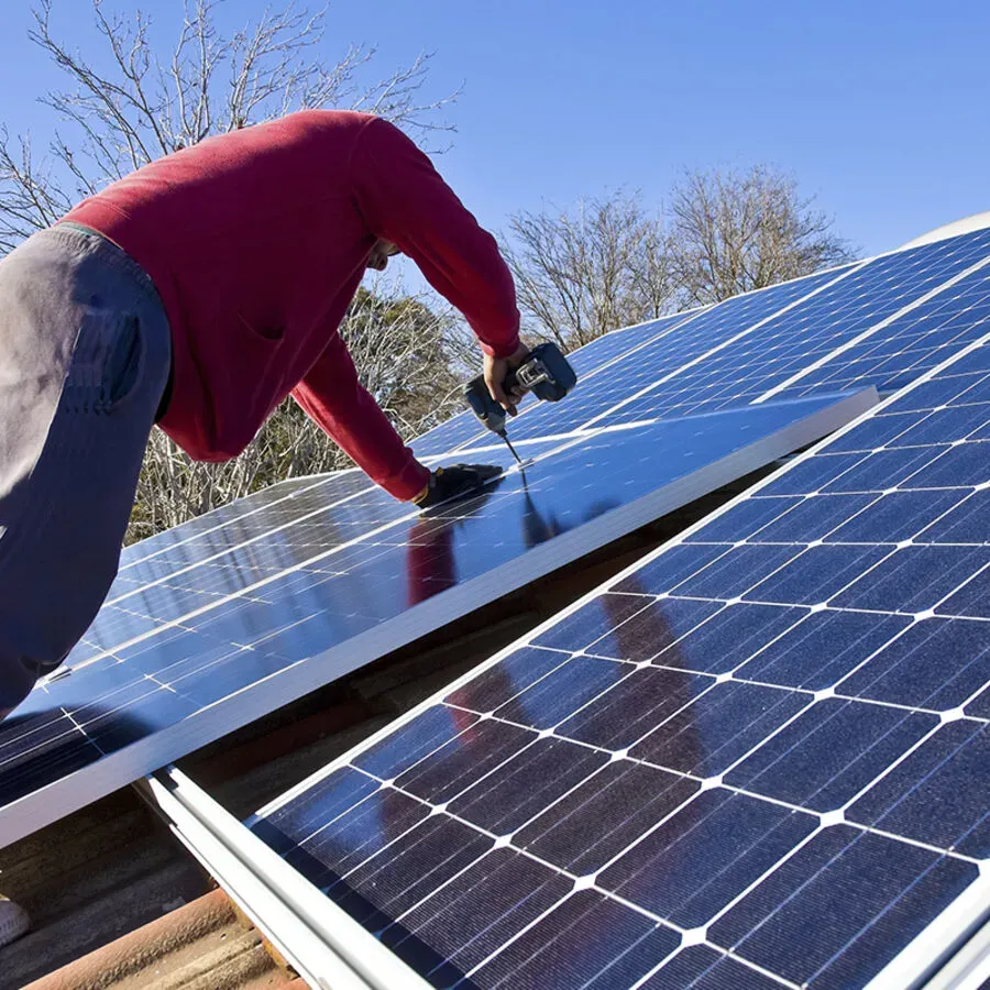 A man in a red shirt is installing solar panels on a roof
