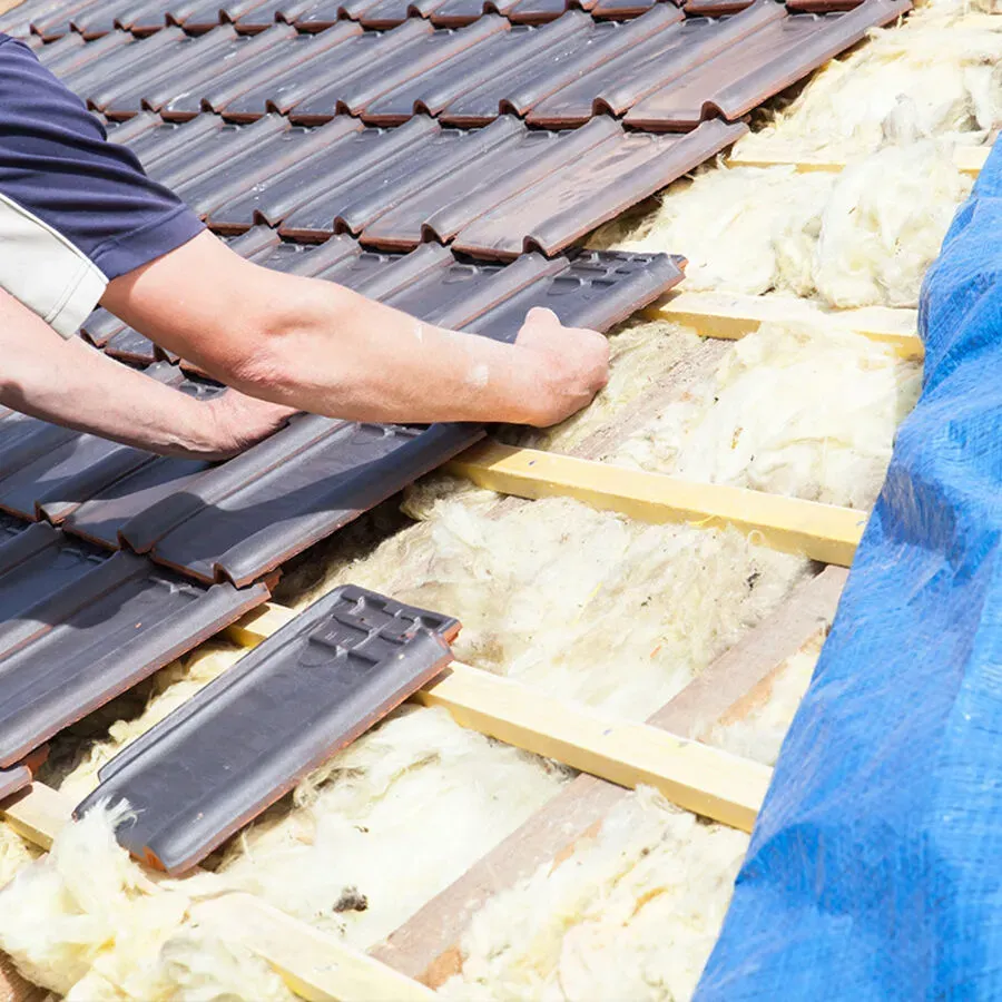 A man is working on a roof with a blue tarp in the background.