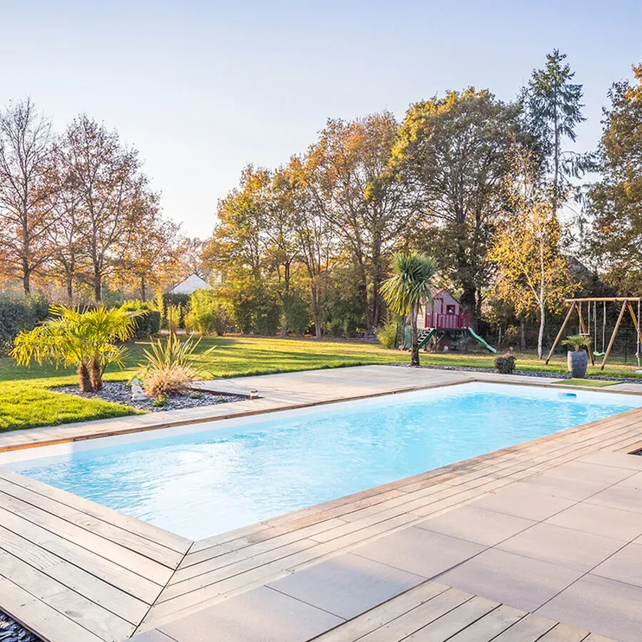 A large swimming pool is surrounded by trees and a wooden deck.