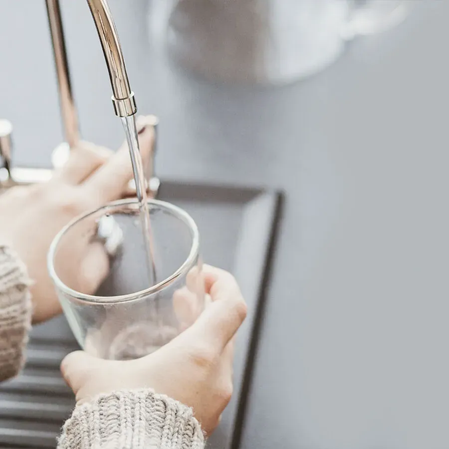 A person is pouring water into a glass from a faucet.