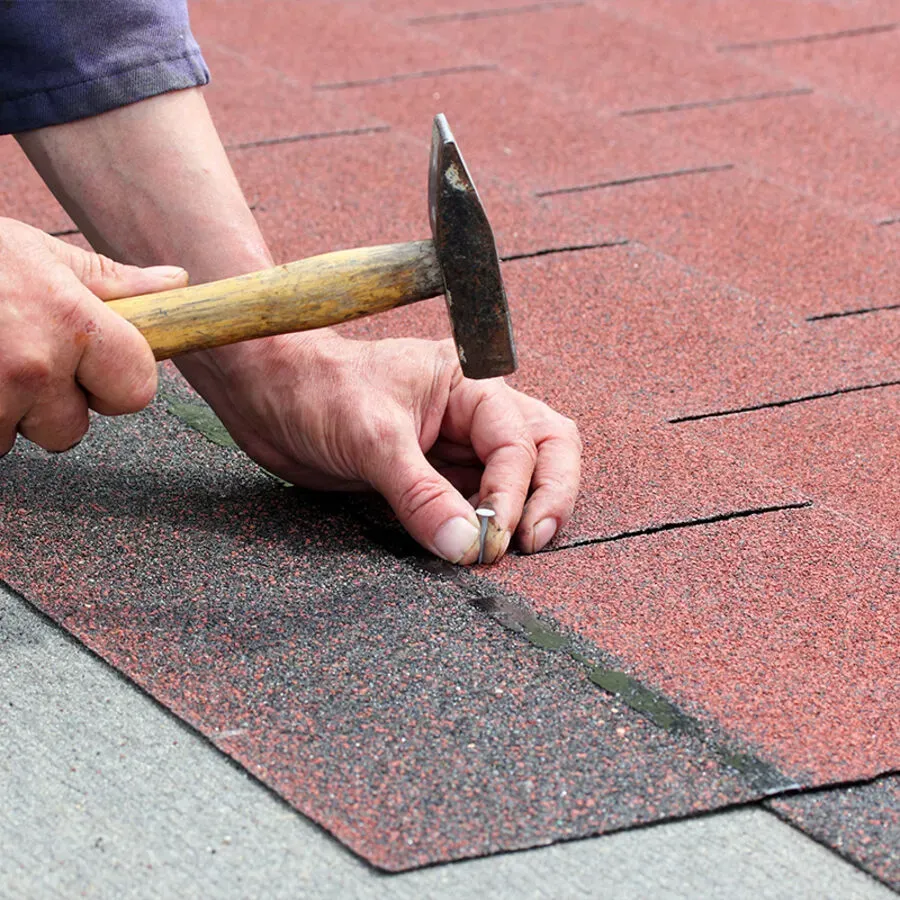 A person is hammering a nail into a roof with a hammer.
