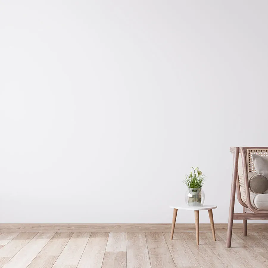 A living room with a white wall , wooden floor , table and chair.