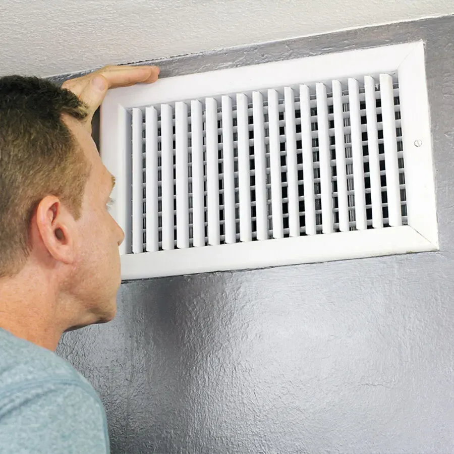 A man is looking at a white air vent on a wall.