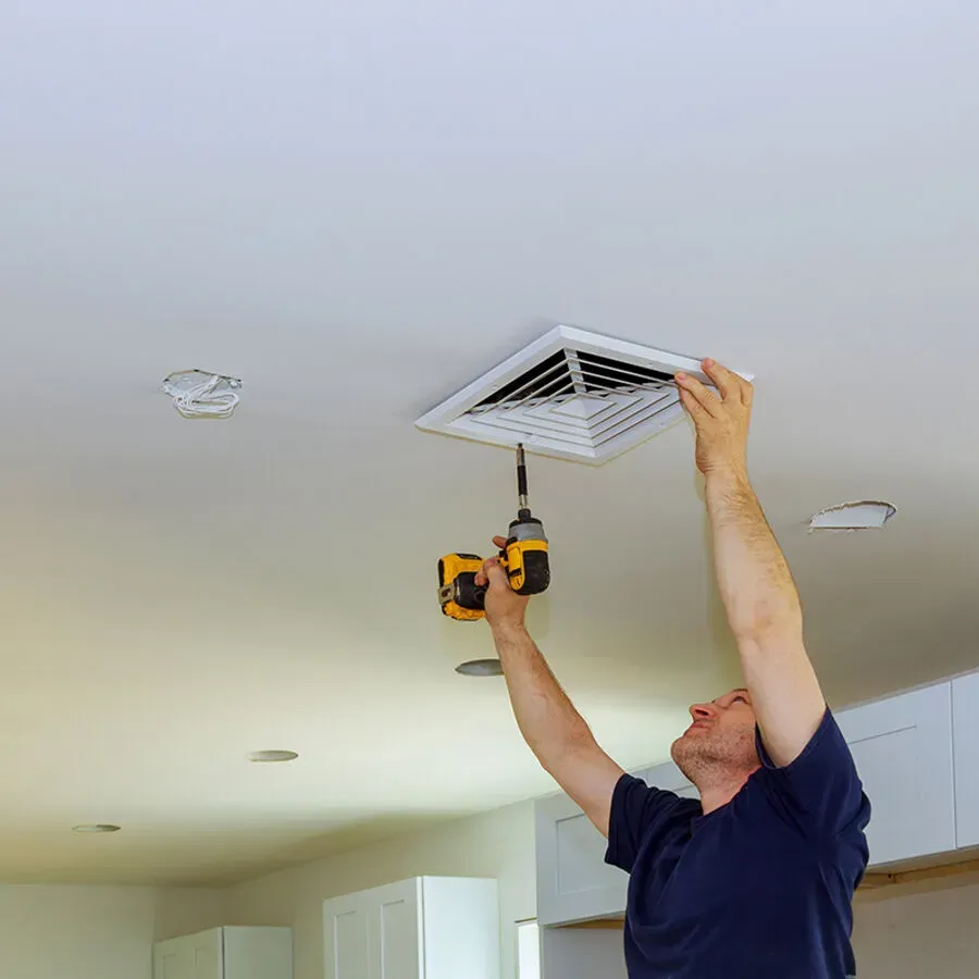 A man is fixing a ceiling vent with a drill.