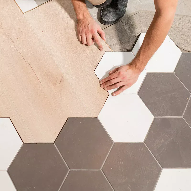 A man is installing a wooden floor with hexagonal tiles.