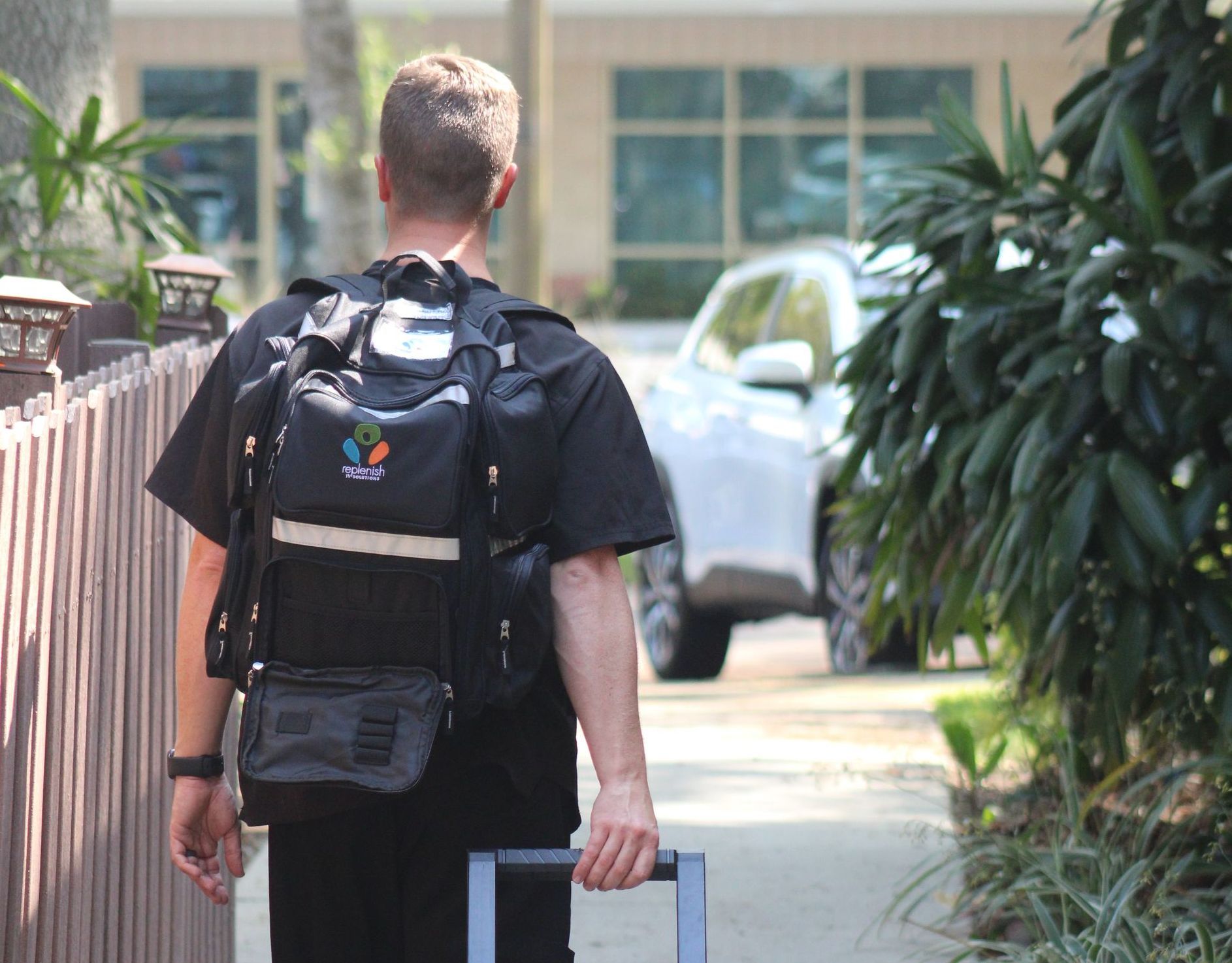 A man with a backpack and a suitcase is walking down a sidewalk.